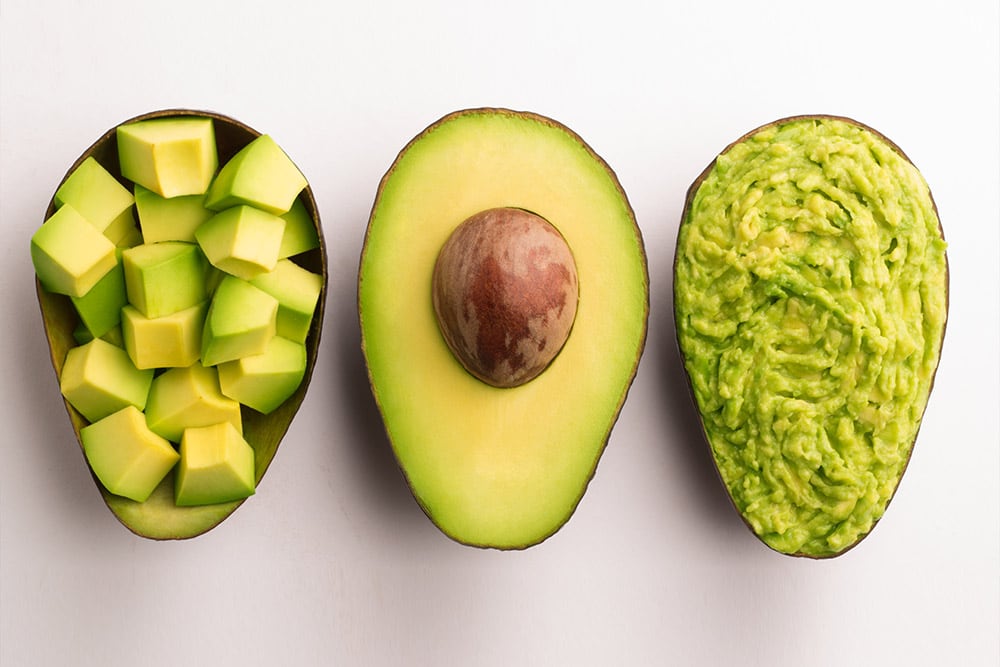 Hass avocado cut open to show its flesh and seed displayed cubed and as guacamole 
