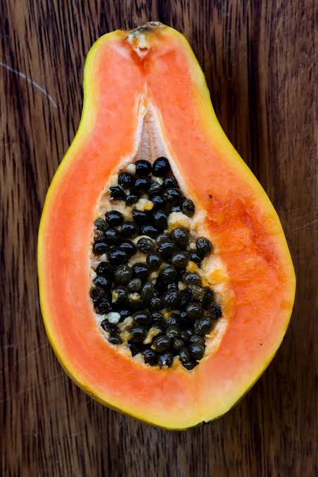 Lengthwise papaya half with salmon-orange flesh and a central cavity containing black seeds.