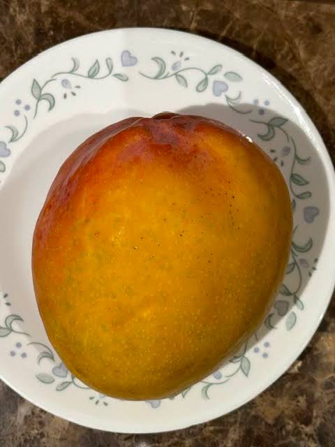 Golden ripe Ugly Betty mango with mottled skin resting on a plate