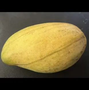 Elongated yellow mango with natural speckles and a faint lengthwise seam resting on a dark surface.